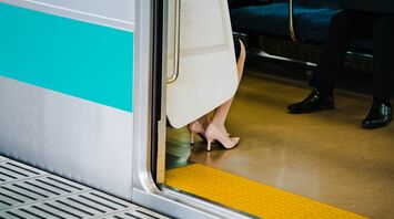 A woman’s legs in heels visible while seated inside a train, with the train door open