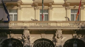 The facade of a historic luxury hotel in Rome with ornate architectural details and flags displayed above its entrance