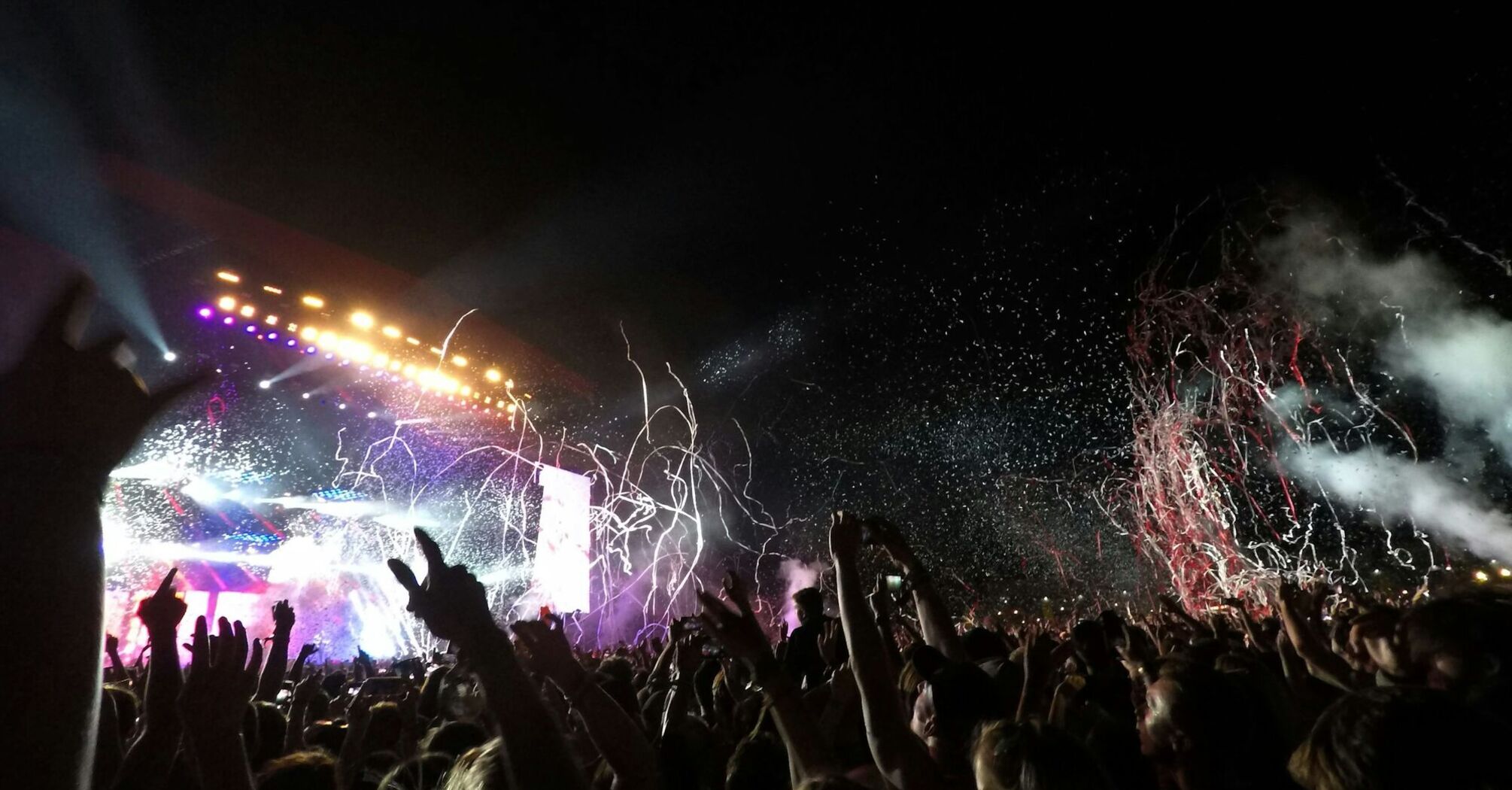 A Reading Festival crowd cheering under vibrant lights at a nighttime concert