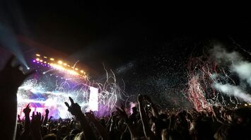A Reading Festival crowd cheering under vibrant lights at a nighttime concert