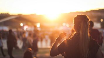 A crowd enjoying a festival at sunset, with a woman in the foreground facing away, capturing the vibrant and warm atmosphere