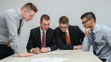 A group of four professionals in business attire discussing documents during a meeting