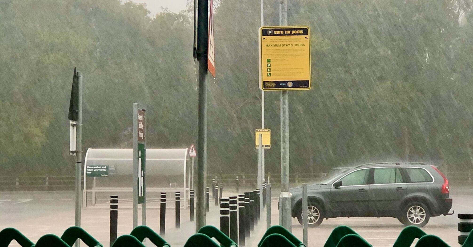 Heavy rain falling in a parking lot with shopping carts and a car in the background