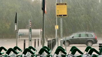 Heavy rain falling in a parking lot with shopping carts and a car in the background