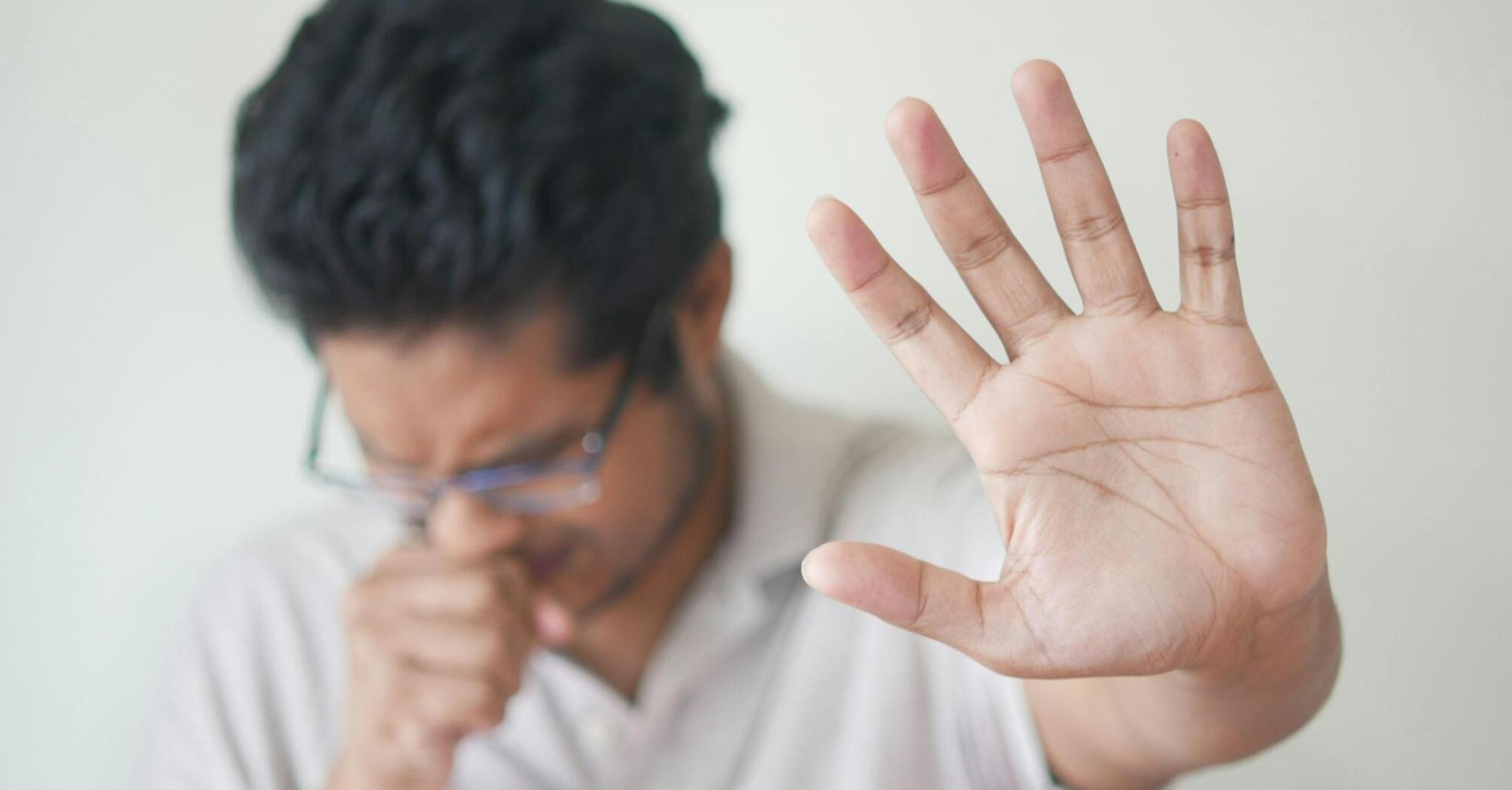 Man coughing with his hand raised in a protective gesture