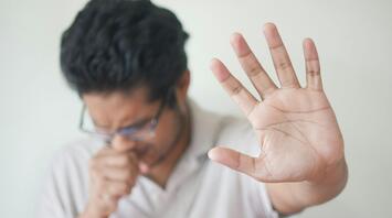 Man coughing with his hand raised in a protective gesture