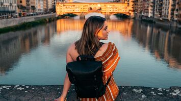 woman in white and orange striped shirt and black leather sling bag siting on gray concrete