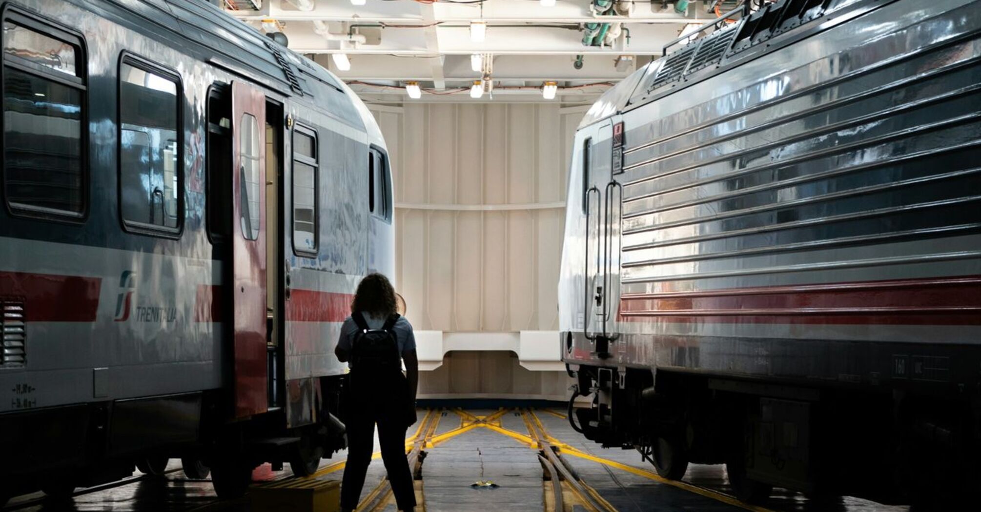 A person stands between two Trenitalia high-speed trains inside a maintenance facility