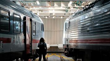 A person stands between two Trenitalia high-speed trains inside a maintenance facility