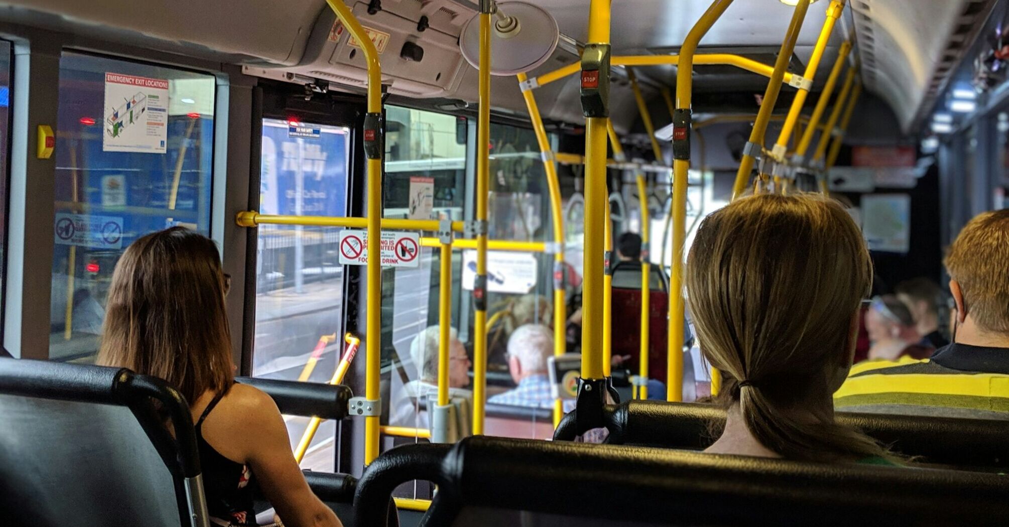 Passengers seated inside a modern bus with yellow handrails and various amenities visible