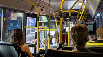 Passengers seated inside a modern bus with yellow handrails and various amenities visible