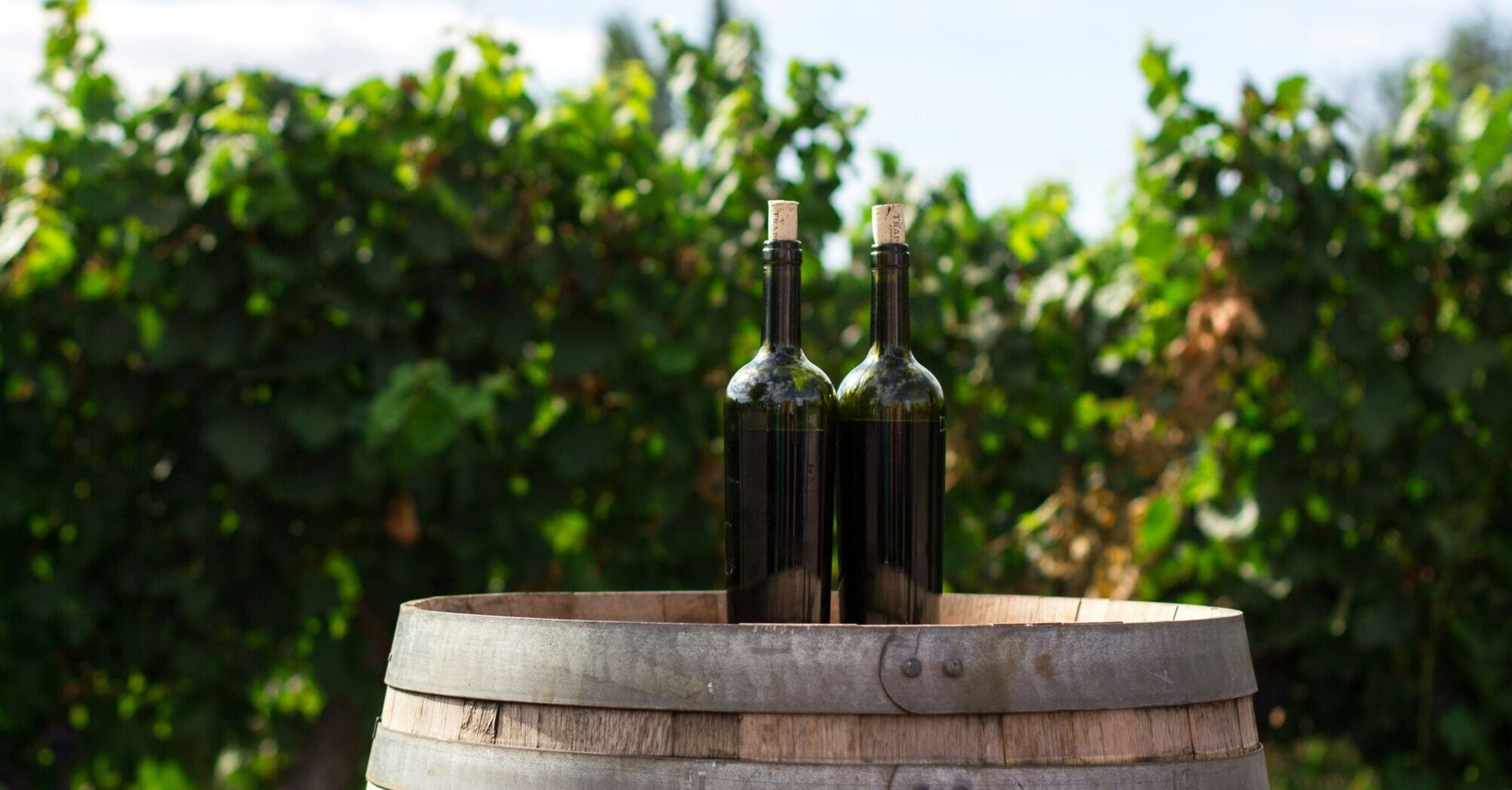 two black wine glass bottles on the top of the brown wooden barrel