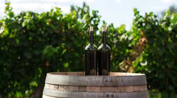 two black wine glass bottles on the top of the brown wooden barrel