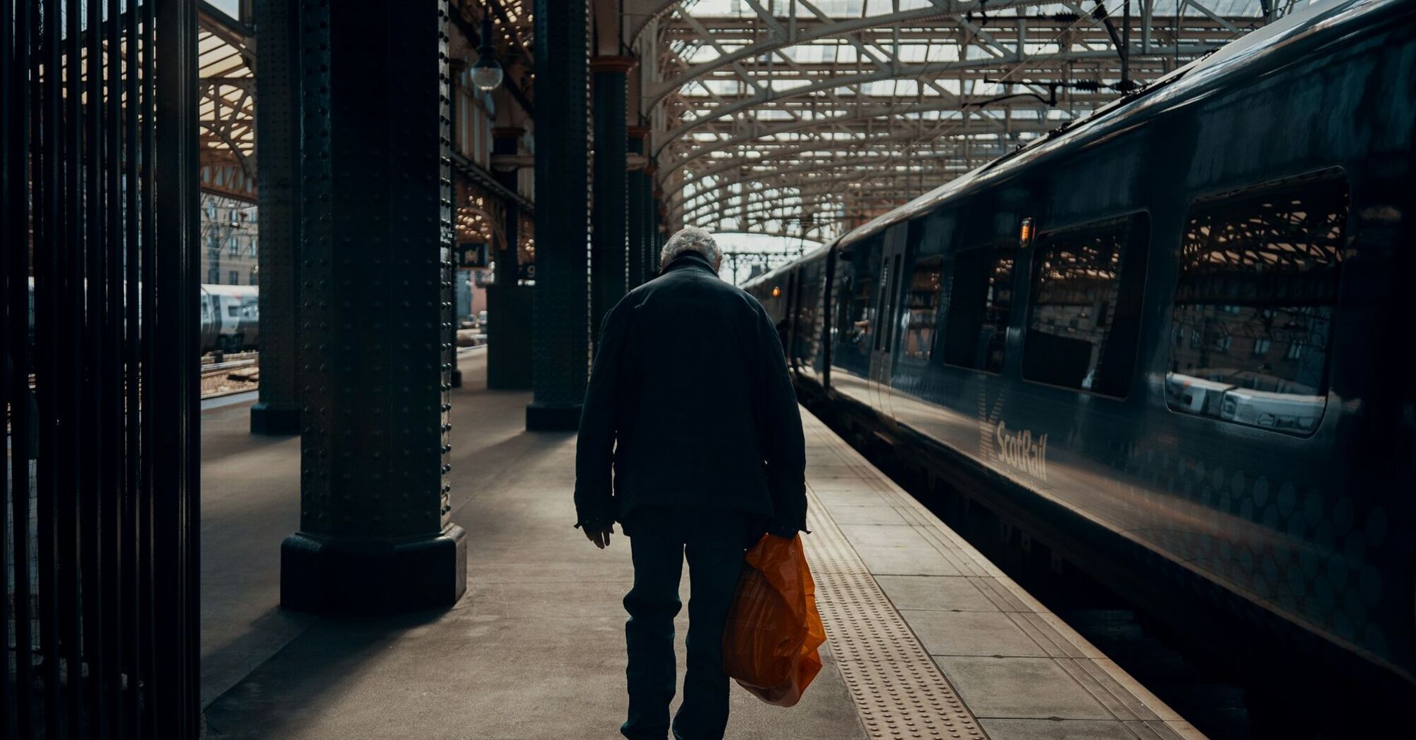 A person with a shopping bag walking along a train platform with a stationary ScotRail train in the background