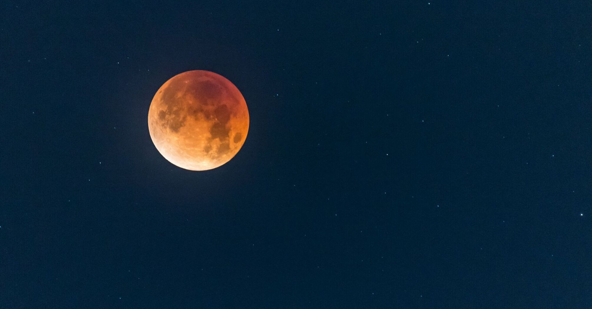 Red-tinted full moon against a starry night sky