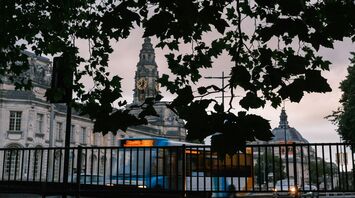 A Stagecoach bus passes by historic buildings in Cardiff, with a clock tower visible through the leaves of nearby trees
