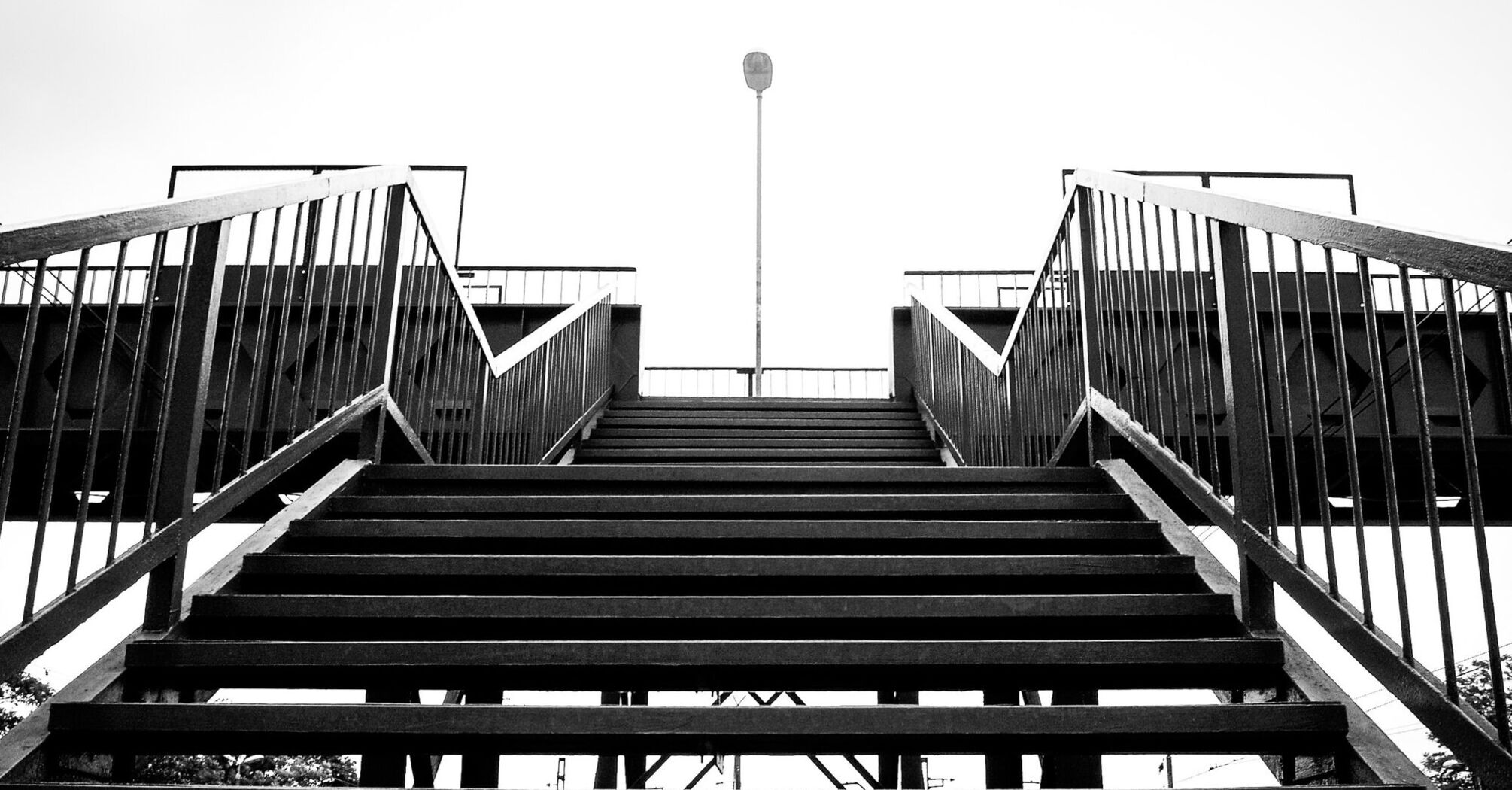 A black-and-white view of a railway footbridge with metal stairs leading up