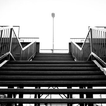 A black-and-white view of a railway footbridge with metal stairs leading up