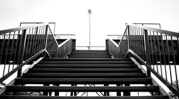 A black-and-white view of a railway footbridge with metal stairs leading up