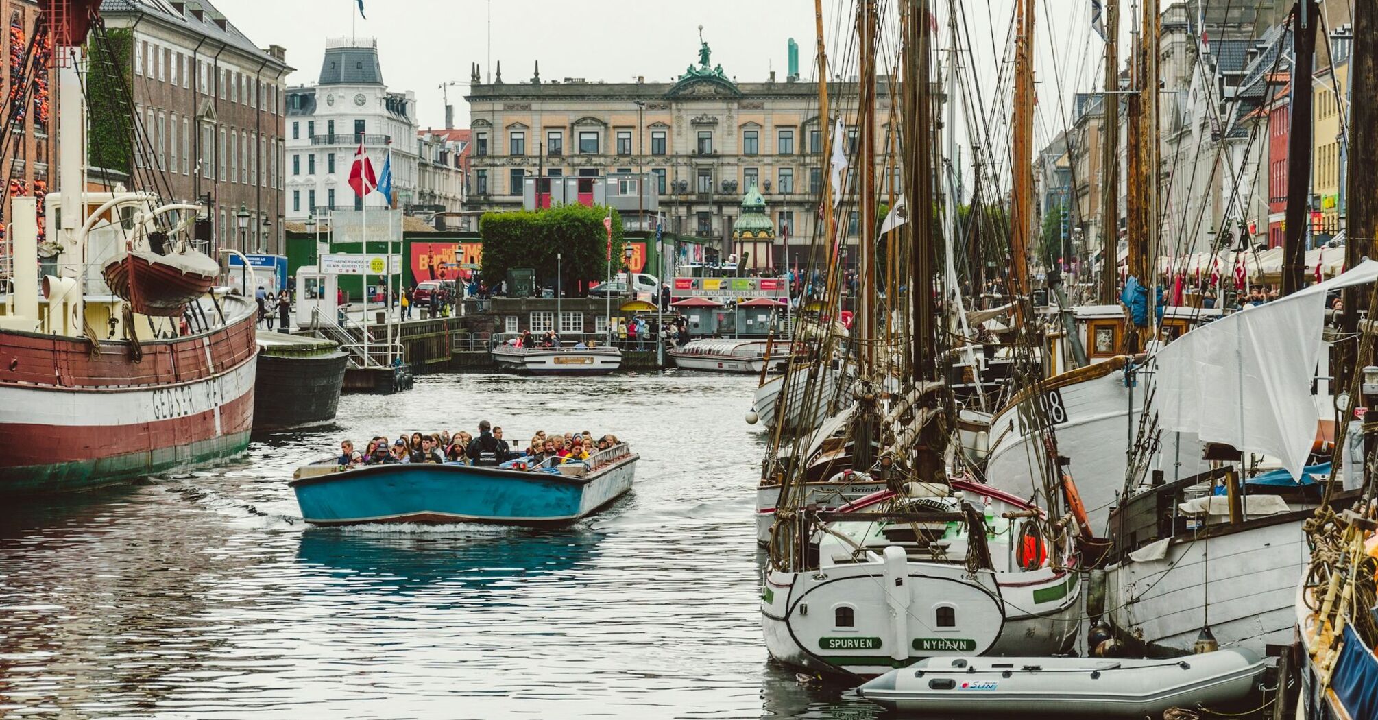 Tourists enjoying a boat ride in a Copenhagen canal surrounded by historic buildings and moored boats