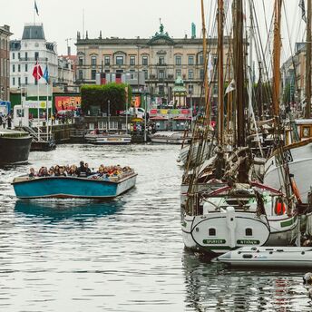 Tourists enjoying a boat ride in a Copenhagen canal surrounded by historic buildings and moored boats