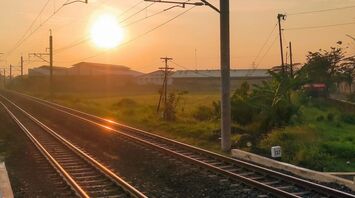 A railway track at sunrise with overhead wires, extending towards the horizon in a rural area