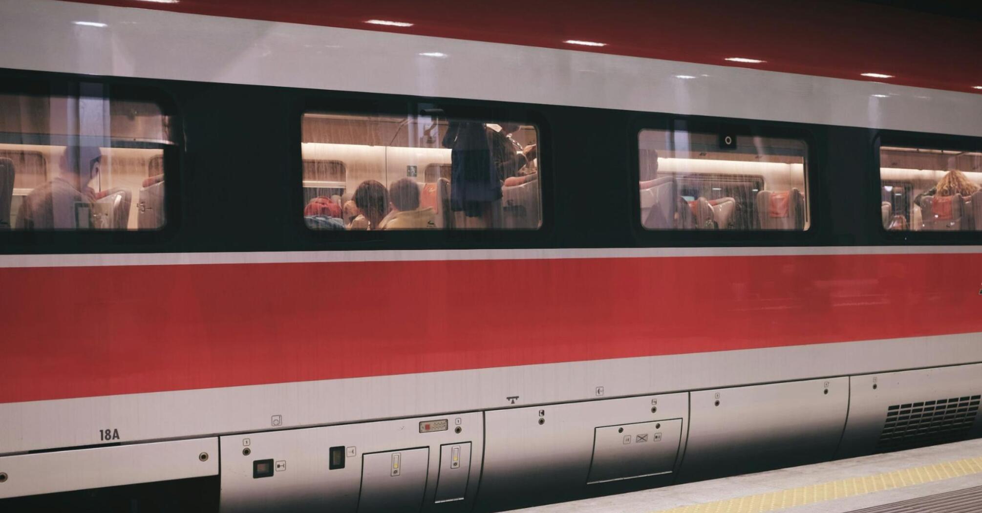 People seated inside a modern red and white train, captured from outside the carriage