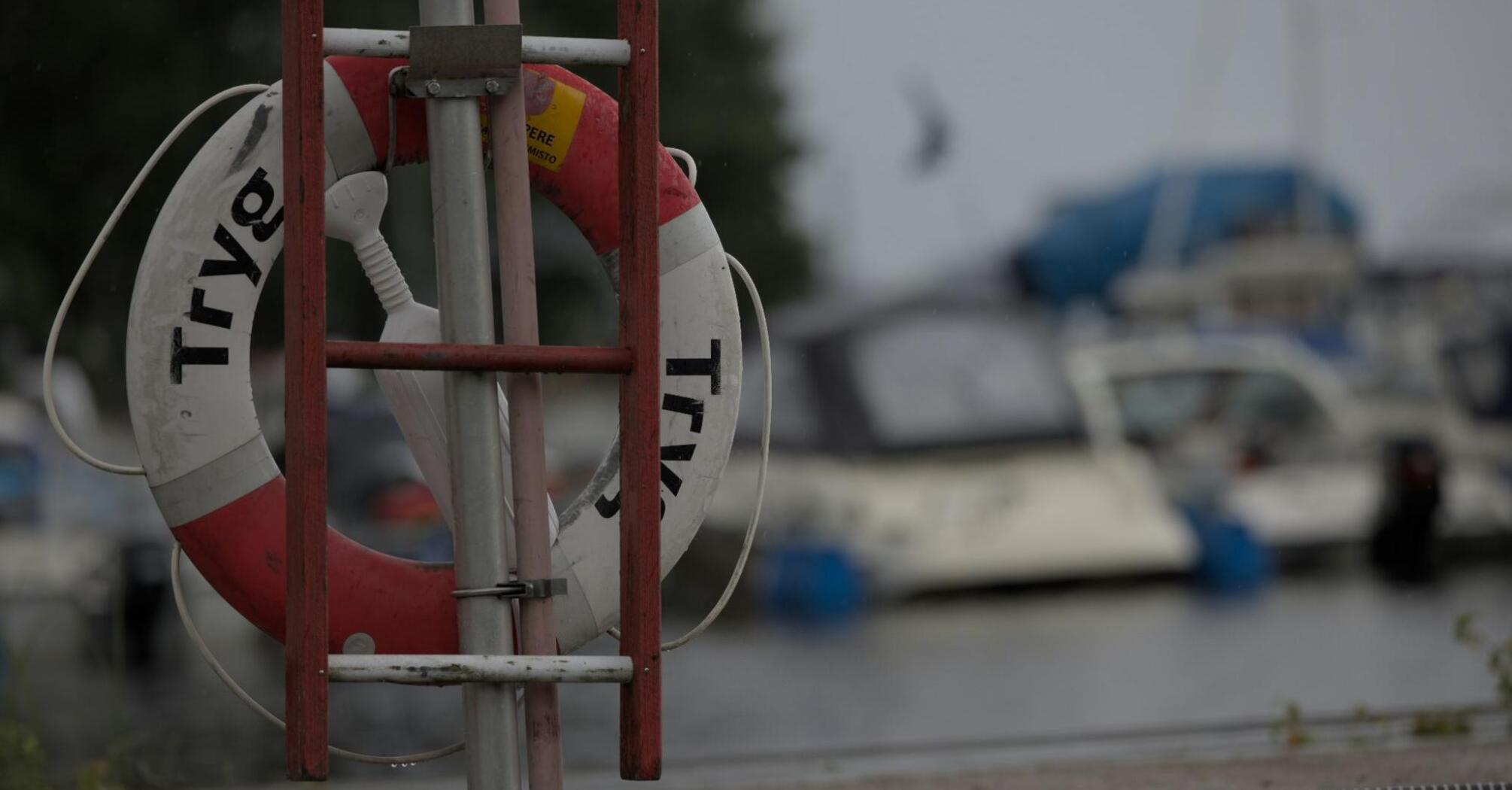 A life preserver mounted on a stand near a harbor with blurred boats in the background