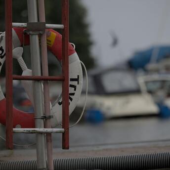 A life preserver mounted on a stand near a harbor with blurred boats in the background