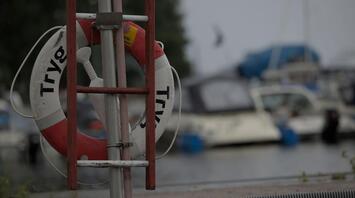A life preserver mounted on a stand near a harbor with blurred boats in the background