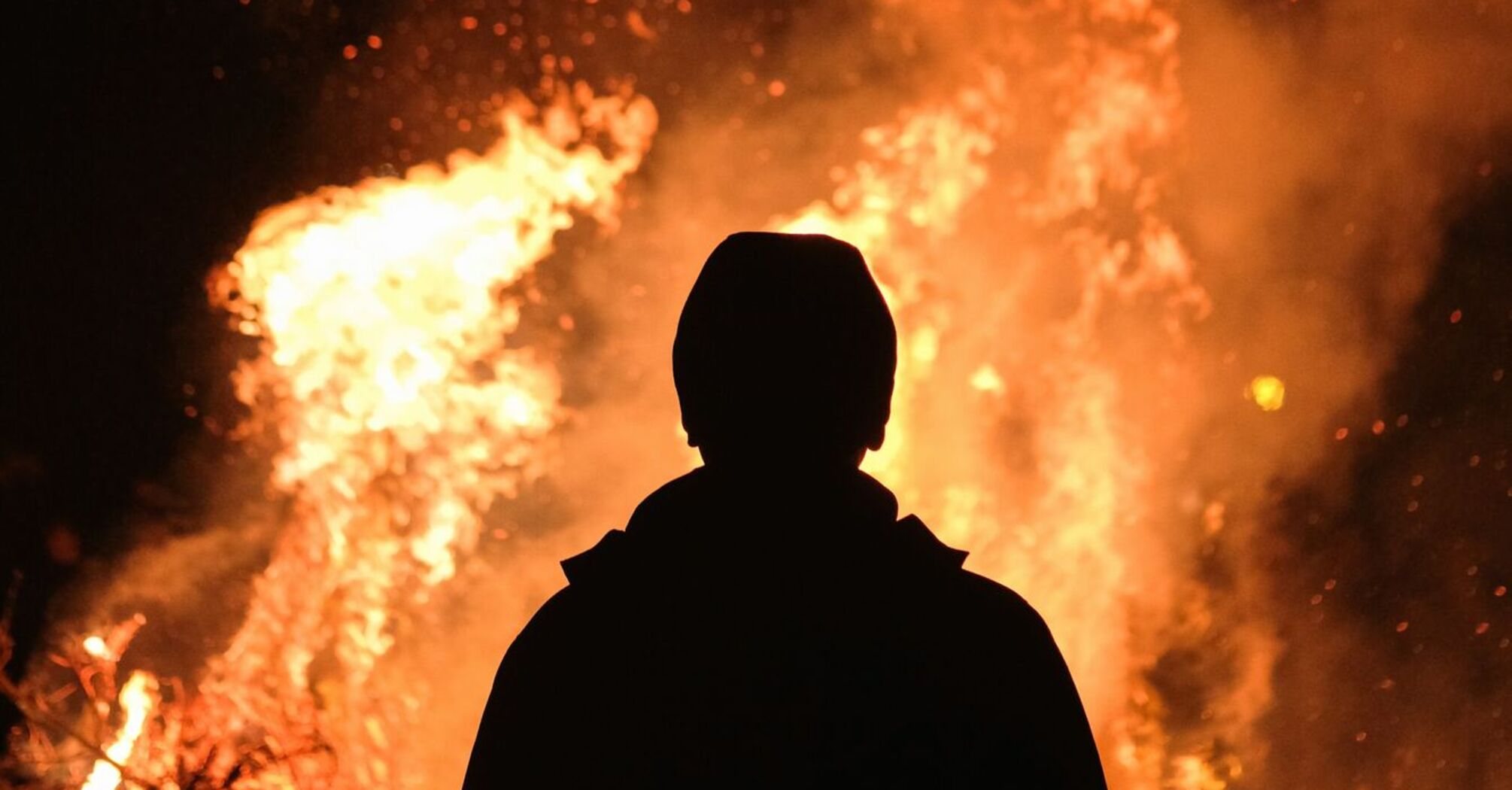 Silhouette of a person standing in front of a large fire