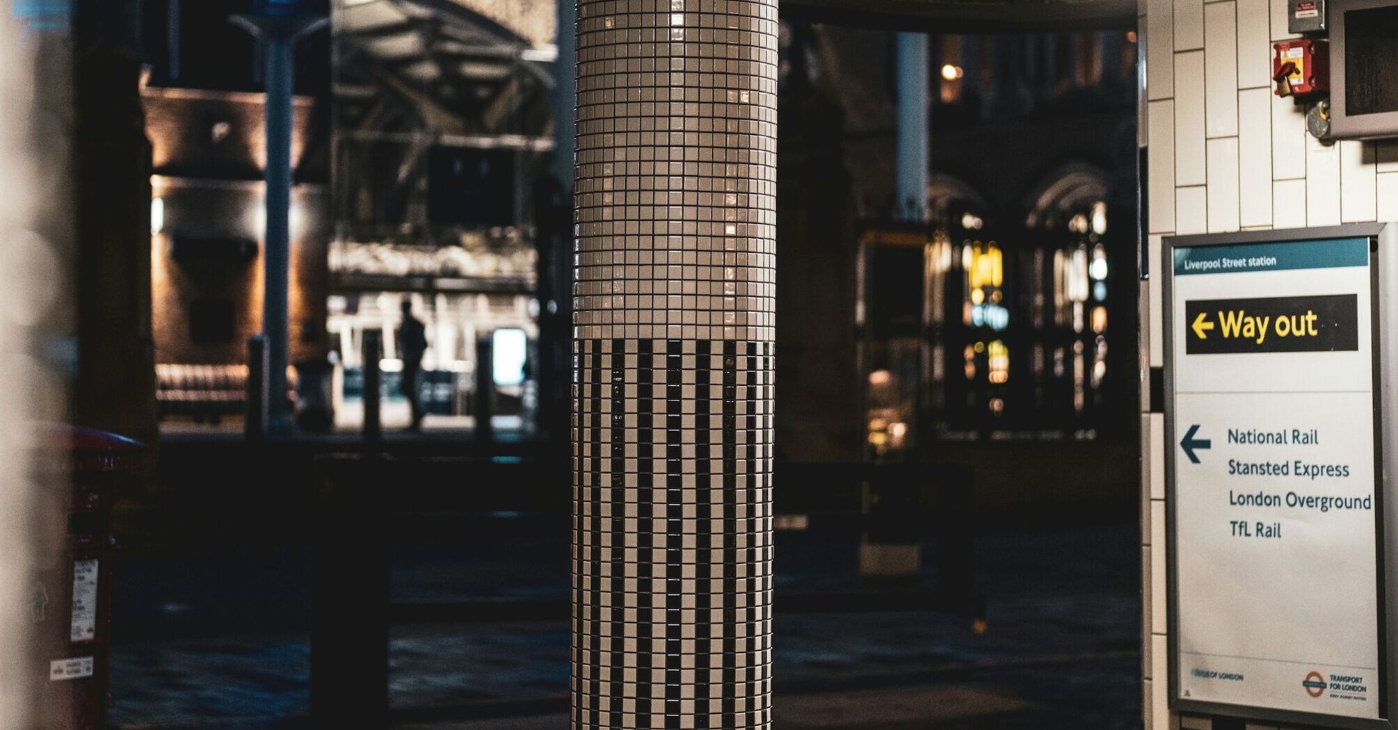 A tiled pillar and station signage at London Liverpool Street station at night