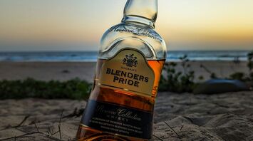 A bottle of whiskey partially buried in the sand at the beach during sunset