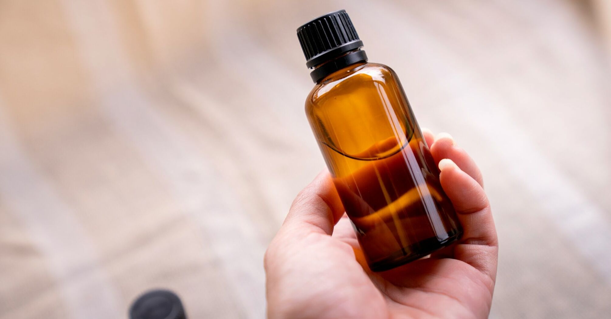 A hand holding a small brown glass bottle