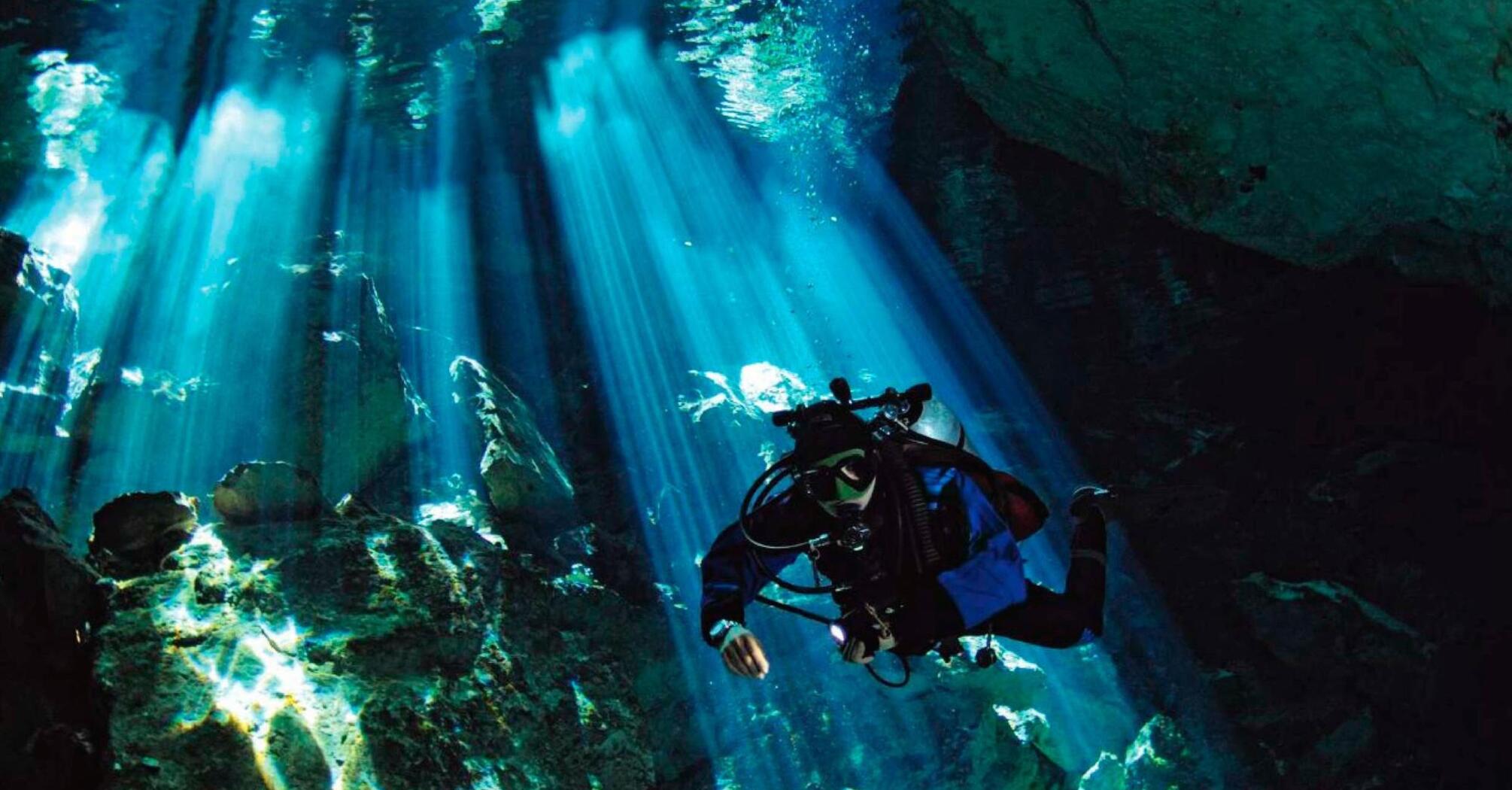 Diver exploring an underwater cave illuminated by sunbeams