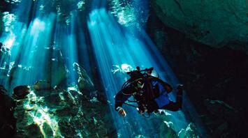 Diver exploring an underwater cave illuminated by sunbeams