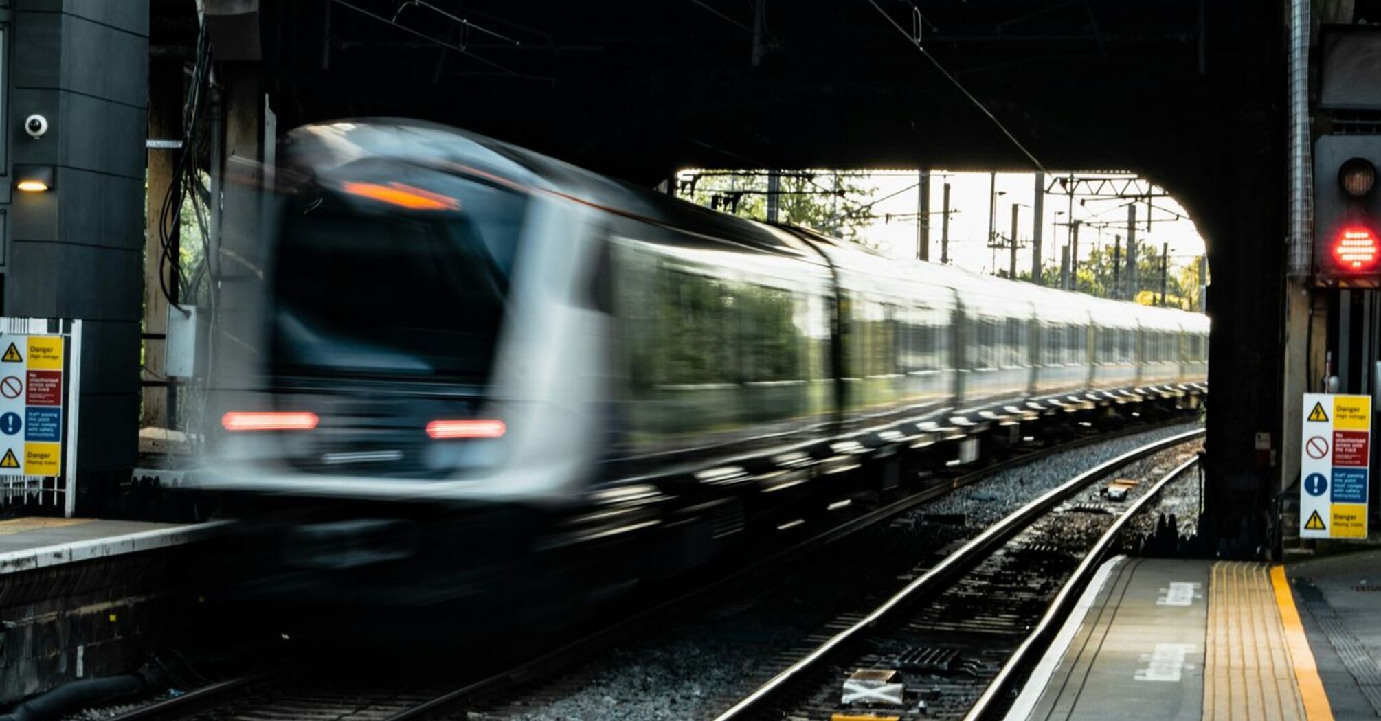 A high-speed train passing through an urban railway station beneath a bridge