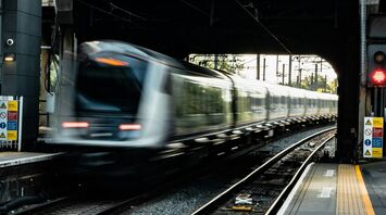 A high-speed train passing through an urban railway station beneath a bridge