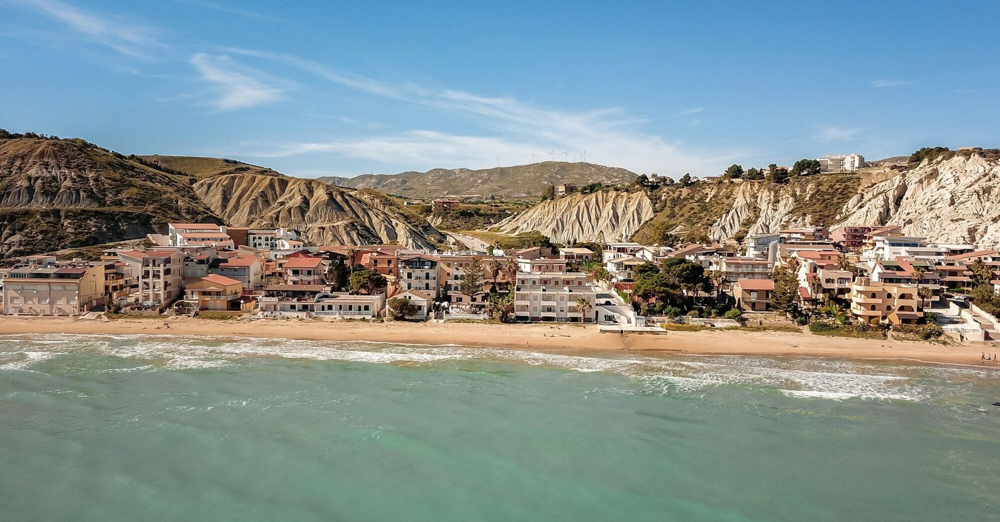 Coastal town in Sicily with beachside houses nestled against rocky hills