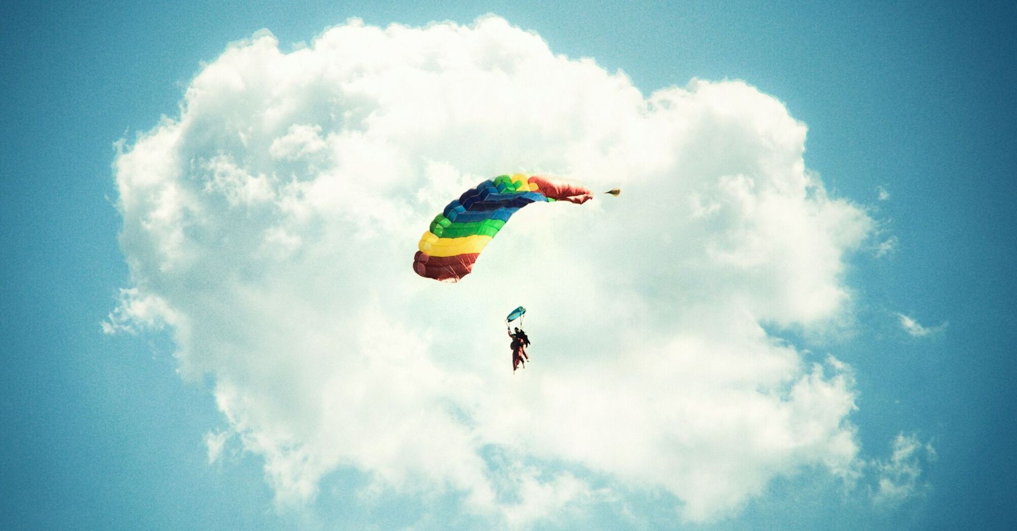 Skydiver with a rainbow parachute against a blue sky