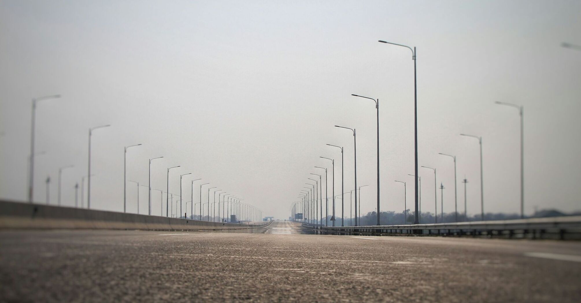 Empty motorway with rows of streetlights extending into the distance under a hazy sky