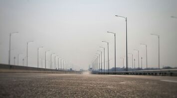 Empty motorway with rows of streetlights extending into the distance under a hazy sky