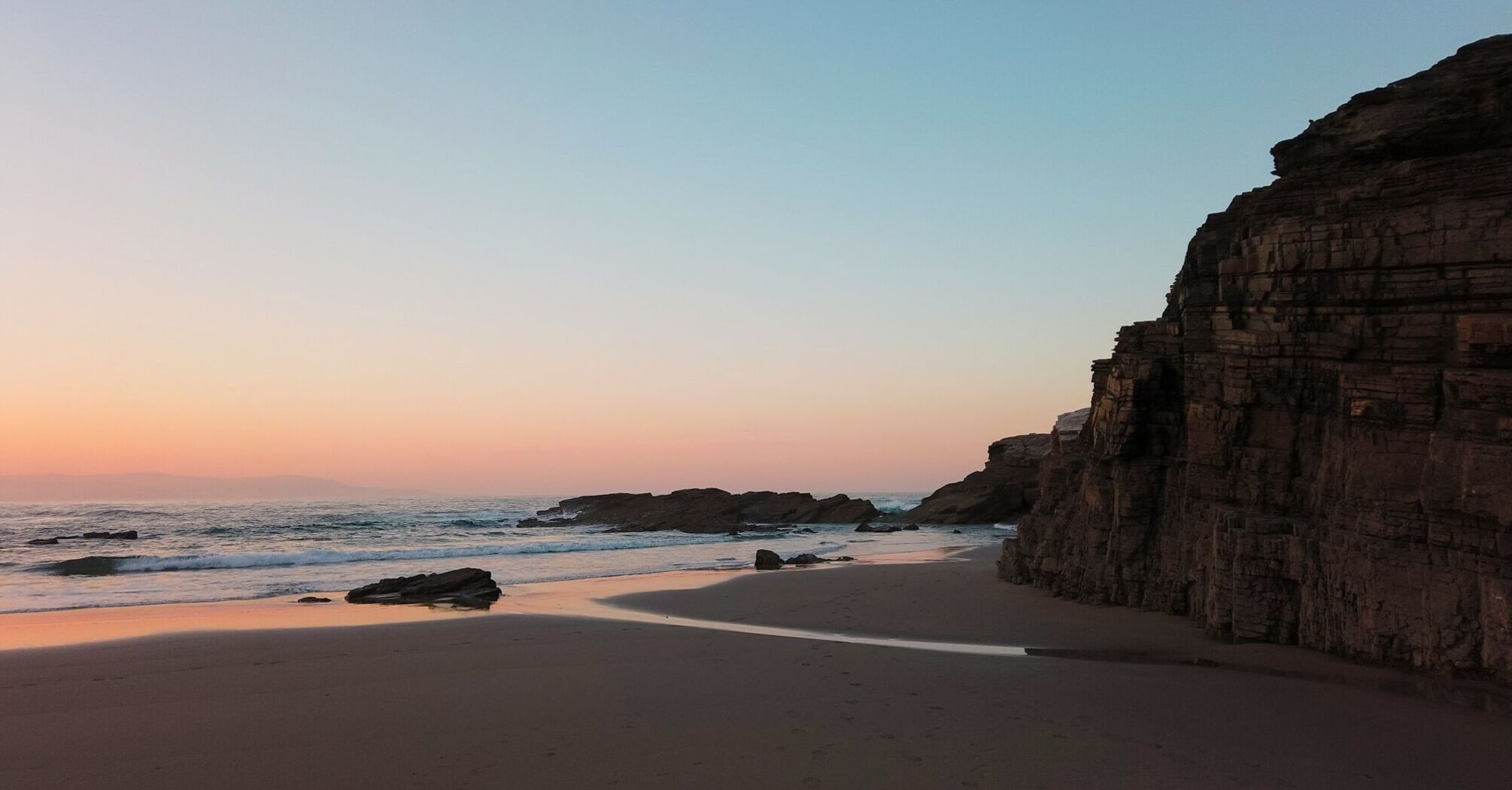 Sunset view of a serene beach with rocks and gentle waves in Galicia