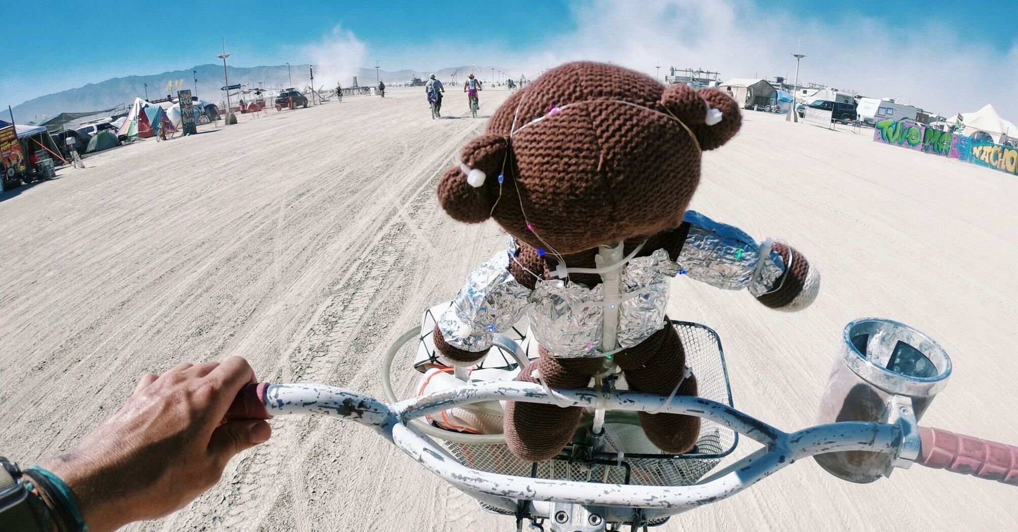 A stuffed toy bear in a shiny outfit on a bicycle in the desert at Burning Man festival