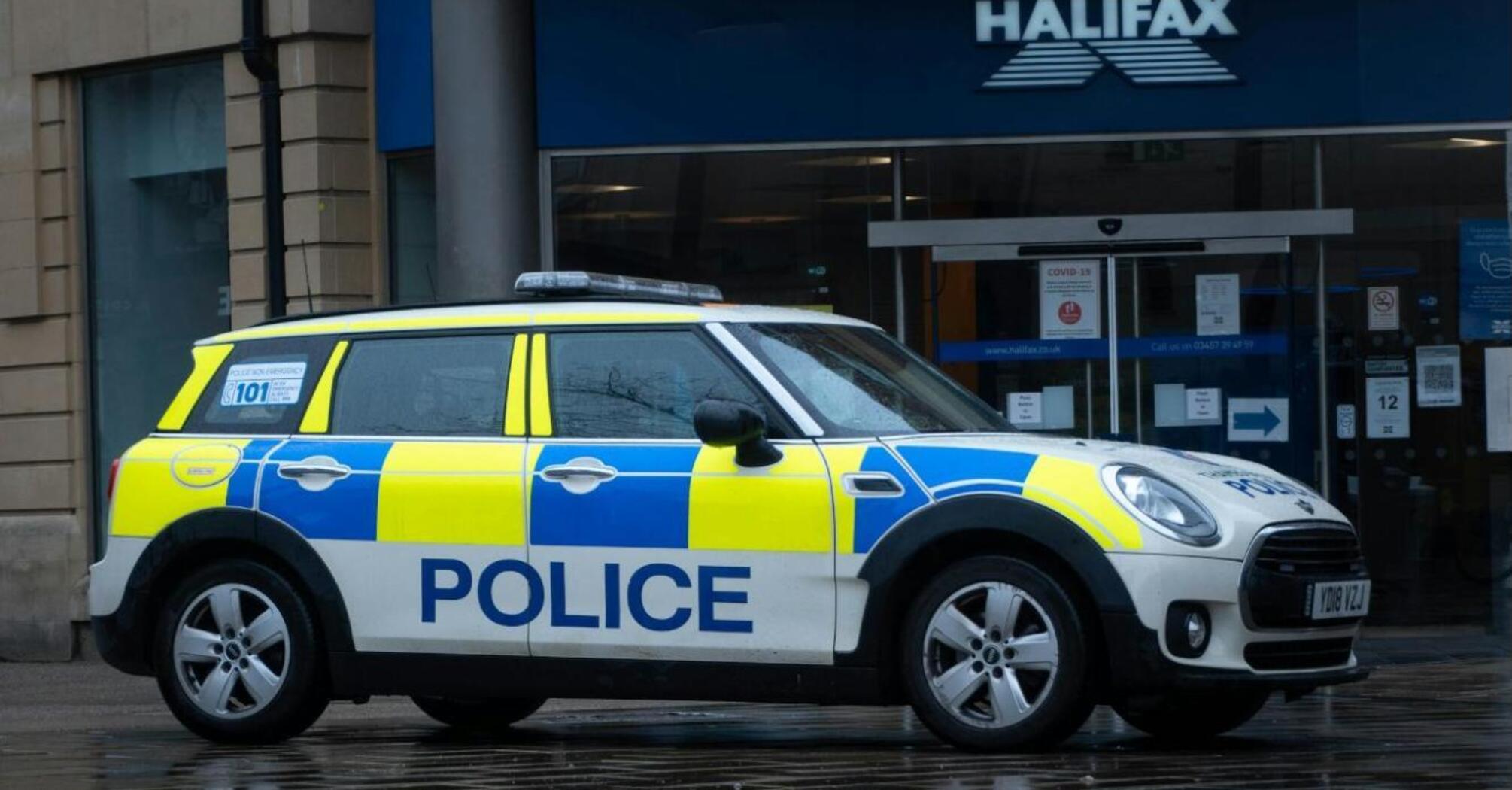 A police car parked outside a Halifax bank on a rainy day, with its reflection visible on the wet pavement