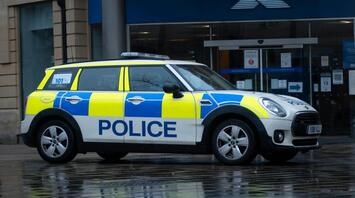 A police car parked outside a Halifax bank on a rainy day, with its reflection visible on the wet pavement