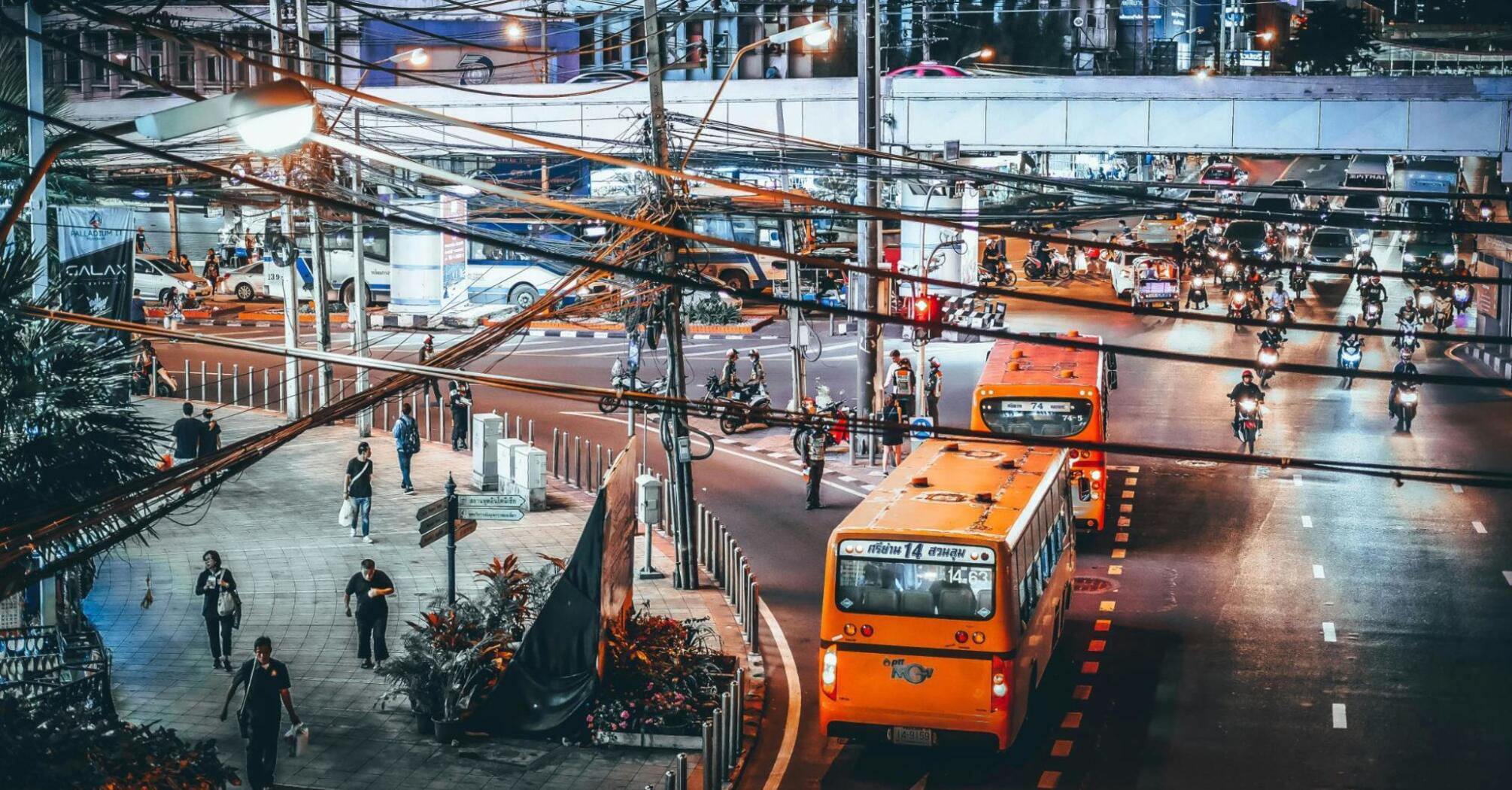 Busy nighttime street in Bangkok with buses, motorcycles, and pedestrians