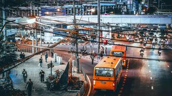 Busy nighttime street in Bangkok with buses, motorcycles, and pedestrians