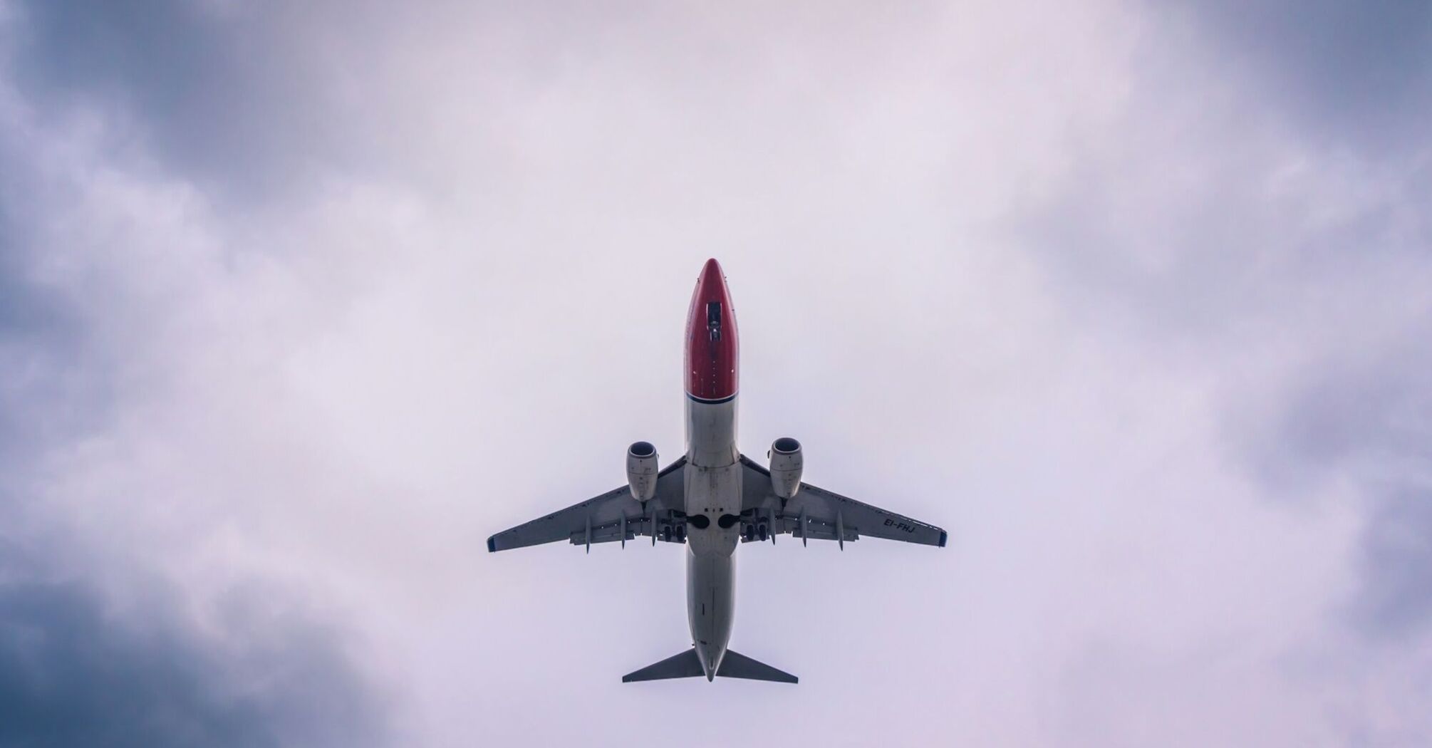 A Norwegian Air aircraft flying overhead against a cloudy sky