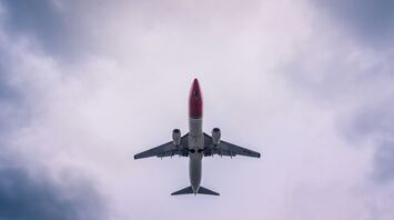 A Norwegian Air aircraft flying overhead against a cloudy sky